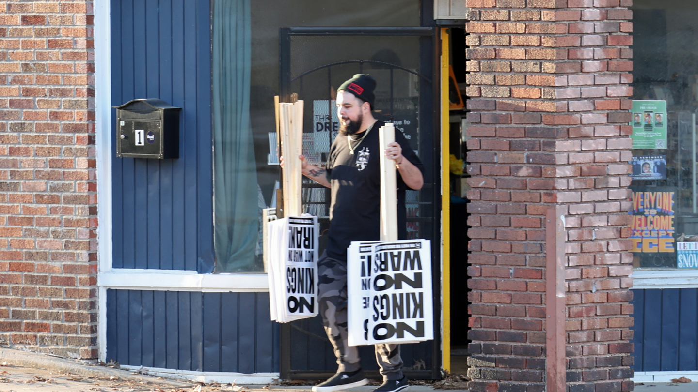 Activist carrying "No Kings — No War on Iran" protest signs